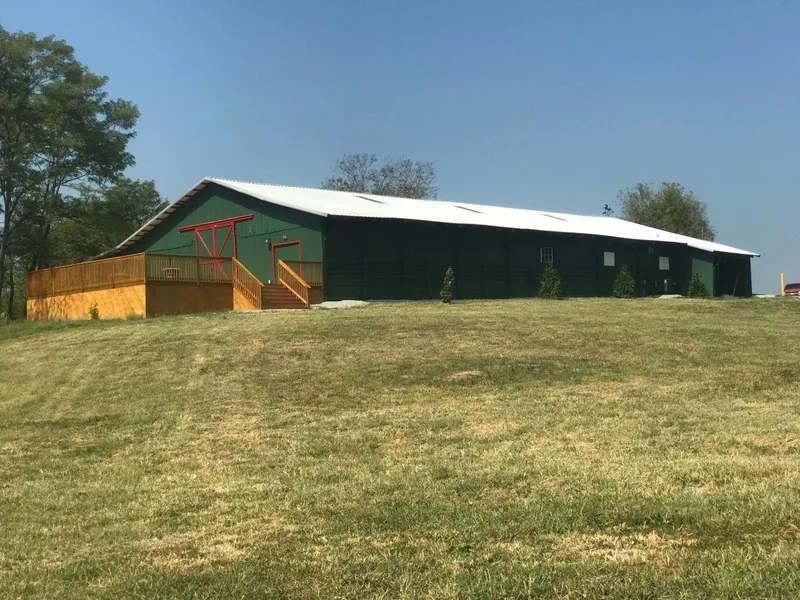 The green barn and its deck on a hill at Land O' Goshen under a blue sky