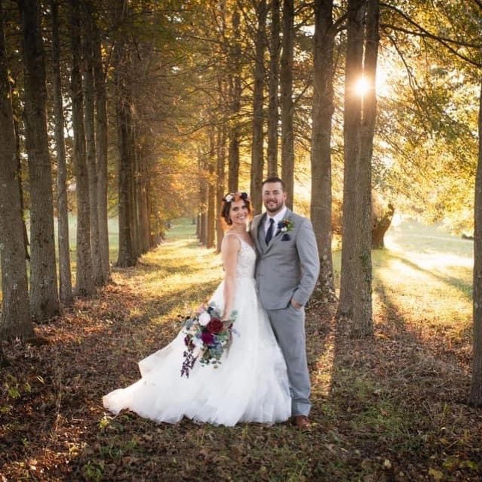 A bride and groom standing on a tree-lined path at sunset on the farm