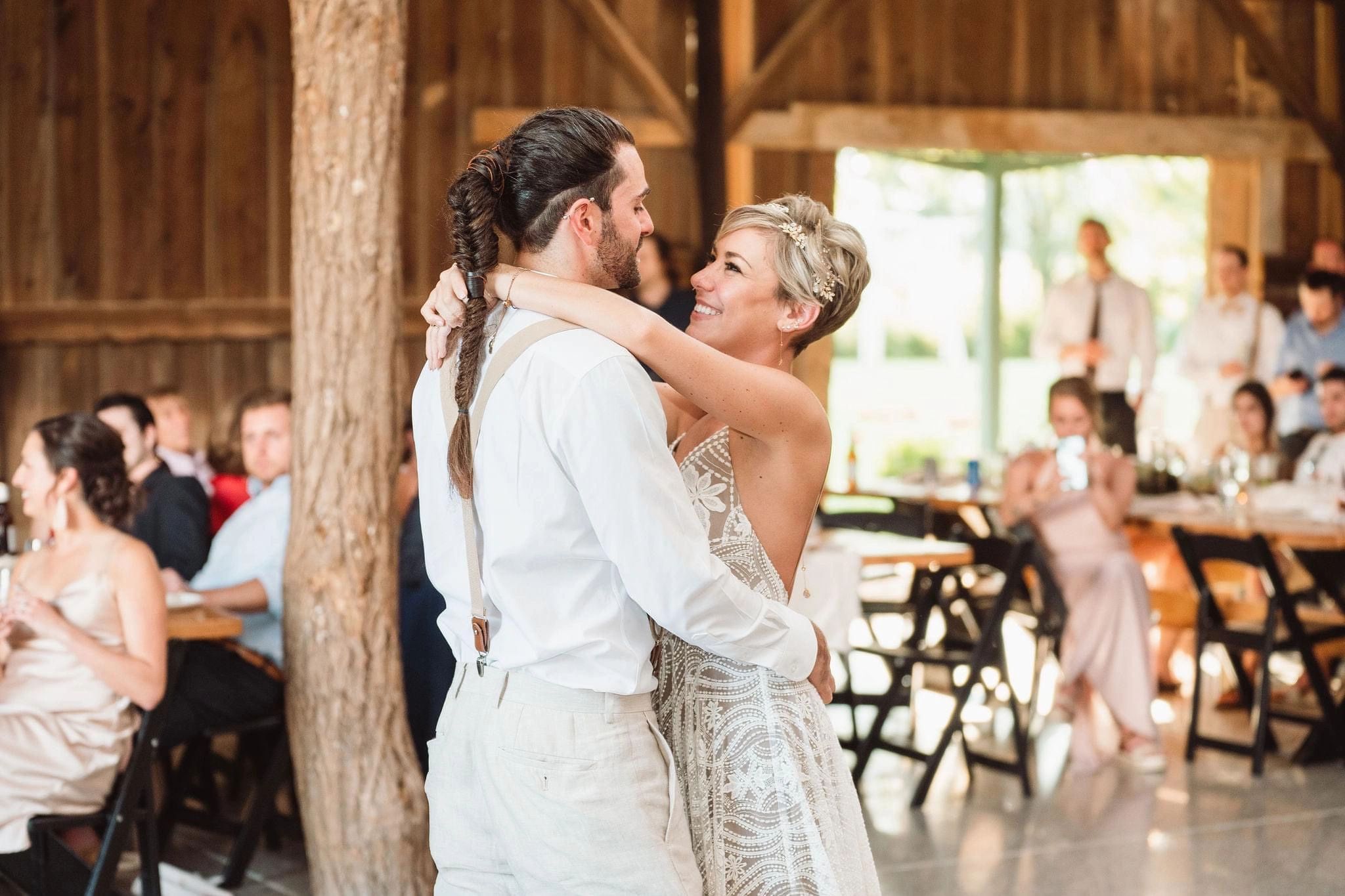 A couple sharing their first dance in the barn with guests watching