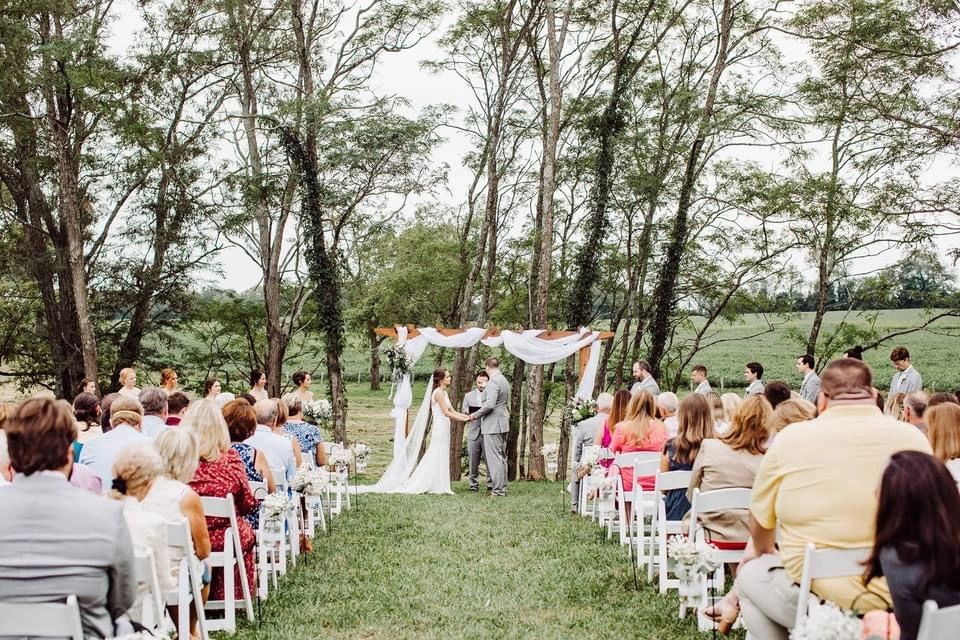 Guests seated on the lawn for an outdoor ceremony under the trees